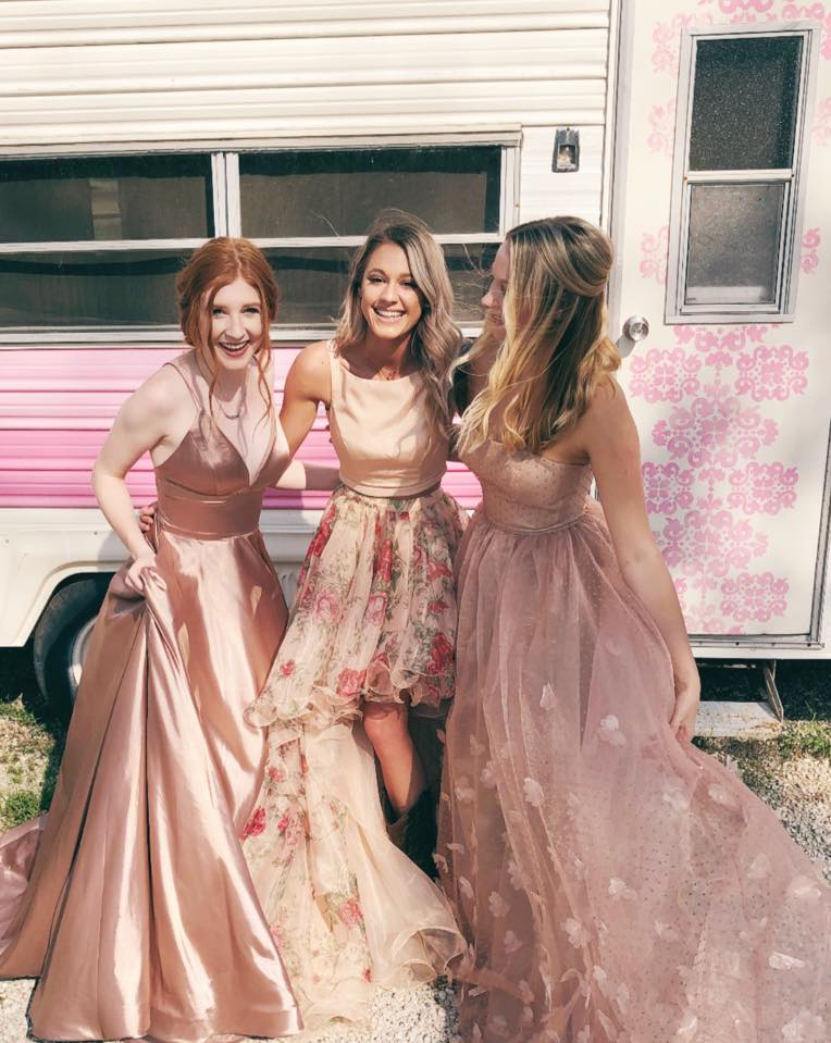 Three girls wearing blush pink homecoming dresses, smiling and laughing. 