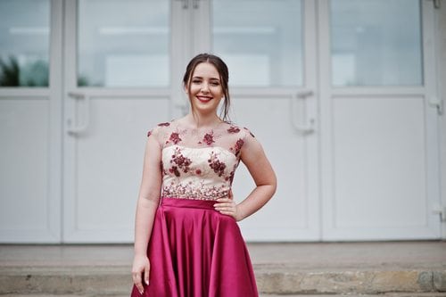 A girl posing in a dark pink prom dress with her hand on her hip.