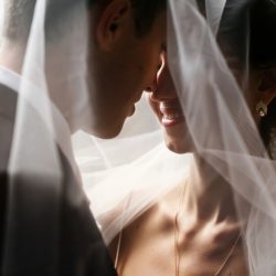 Bride and groom smiling under veil, noses touching